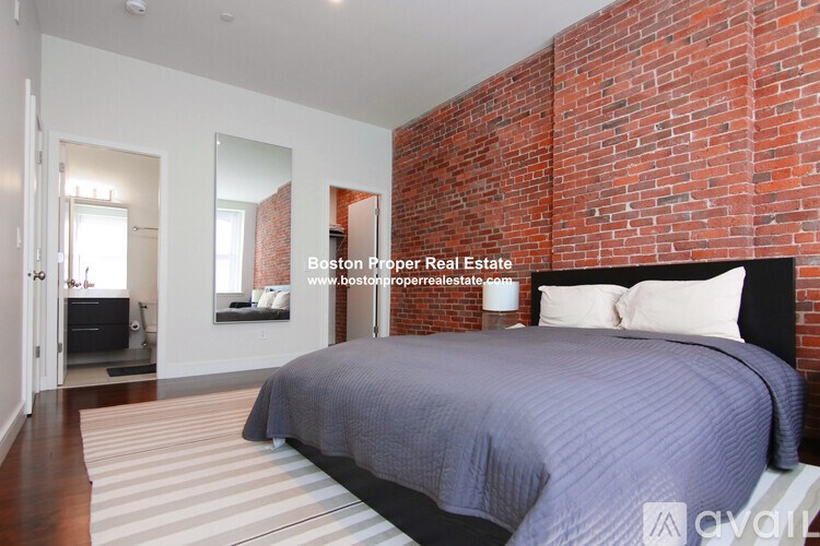 A bedroom with a brick wall and a bed with a blue comforter.