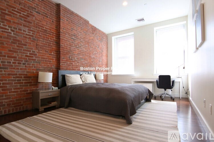 A bedroom with a brick wall and a bed with a brown comforter.