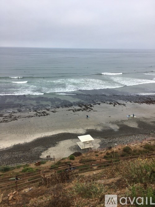 A beach with waves crashing onto the shore and a small building in the distance.