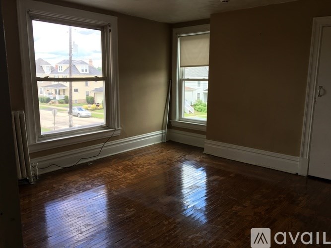 A room with wooden floors and two windows, one of which has blinds.