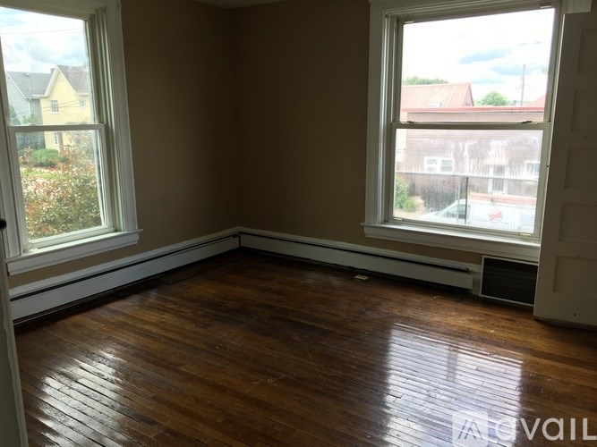 A room with brown walls and wooden floors, with two windows letting in light.
