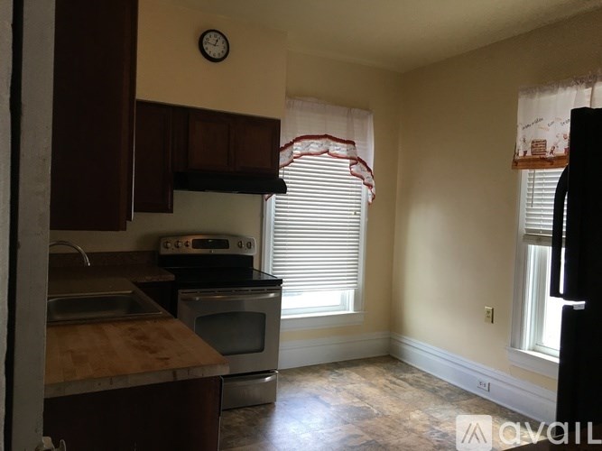 A kitchen with a clock on the wall and a window with blinds.