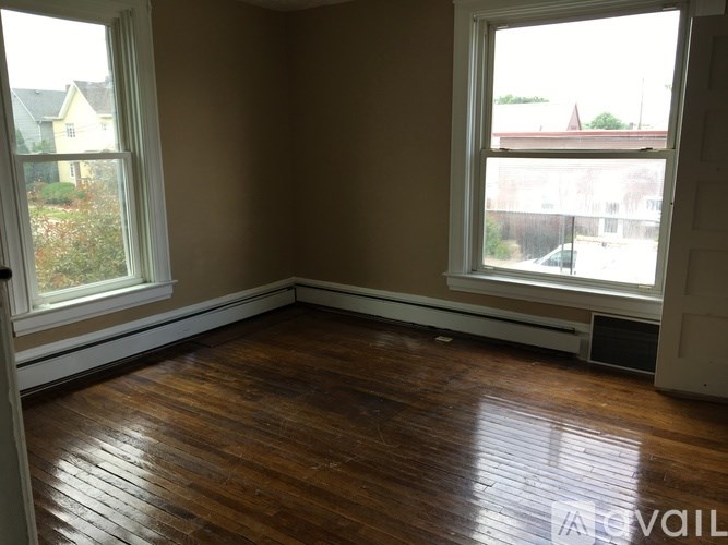 A room with brown walls and wooden floors has two windows.