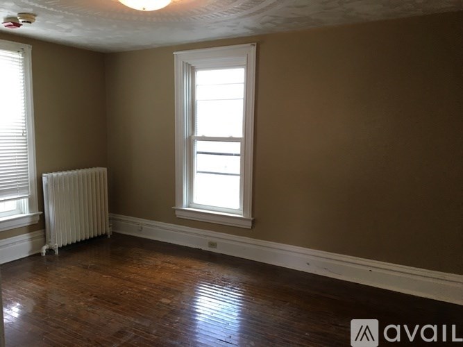 A room with brown walls, a window, a radiator, and wooden flooring.