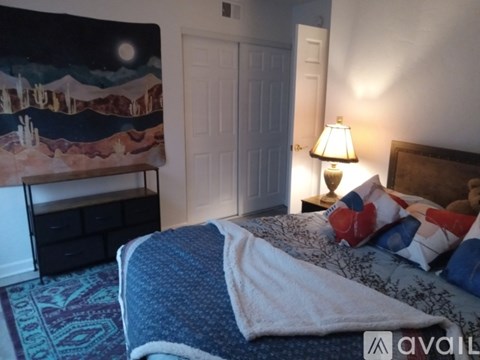 A bedroom with a bed, a nightstand with a lamp, and a painting on the wall.