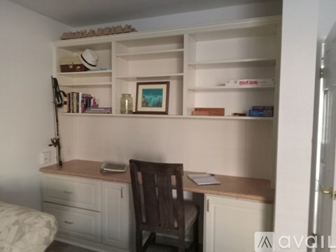 A room with a desk, chair, and shelves with various items.
