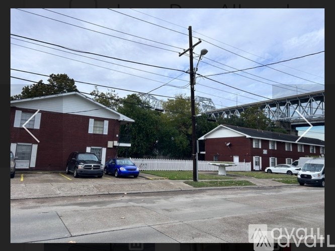 A red brick building with a white door and windows, a black car parked in front, and a blue car parked behind it.