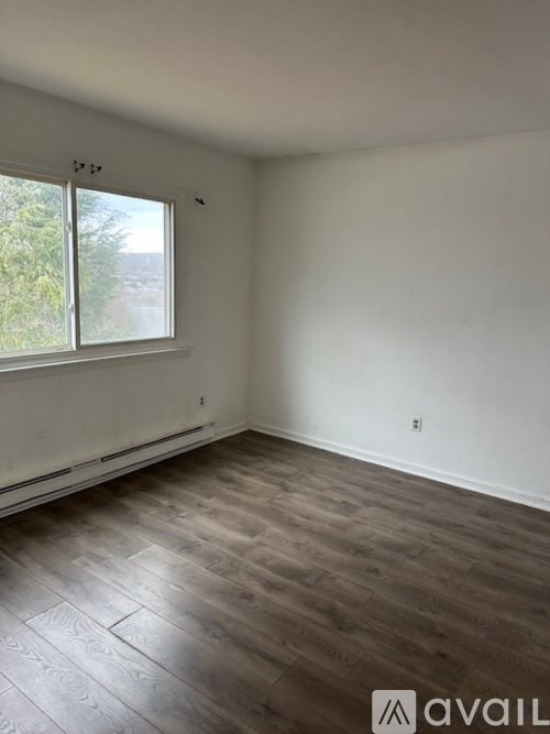A room with wooden flooring and a window overlooking trees.