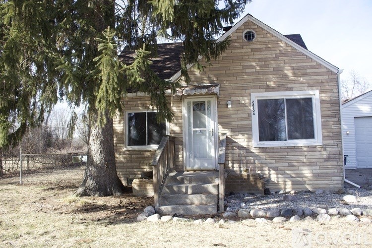 A small house with a porch and a tree in front.