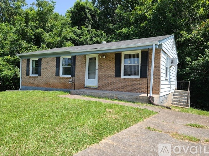 A small brick house with a porch and a green lawn in front.