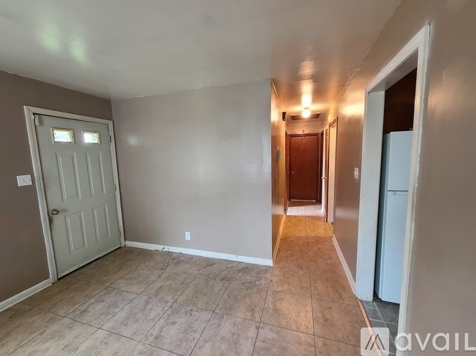 A room with a door on the left and a refrigerator on the right.