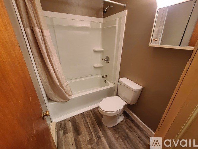 A small bathroom with a toilet, a shower with a glass door, and a wooden floor.
