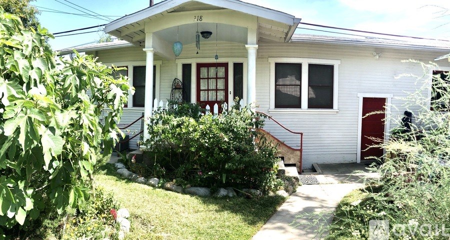 A white house with a red door and a green bush in front.
