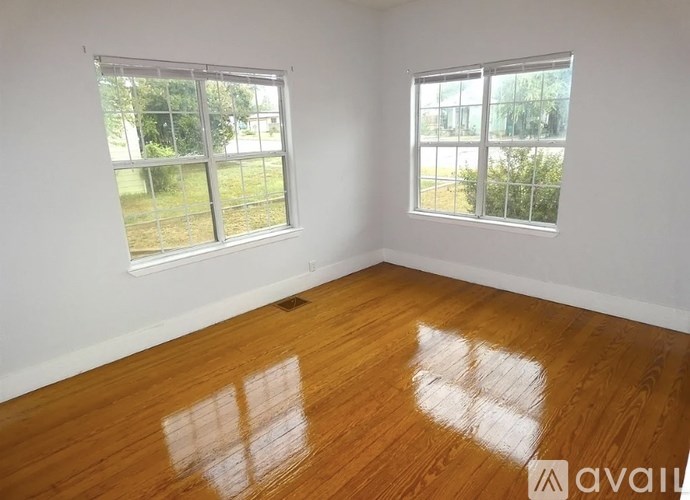 A room with wooden floors and two windows overlooking a green area.