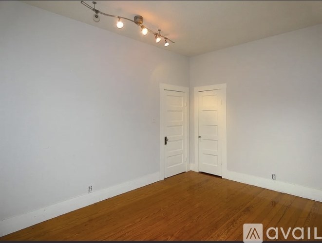 A room with wooden floors and white walls, with a door on the left and a window on the right.