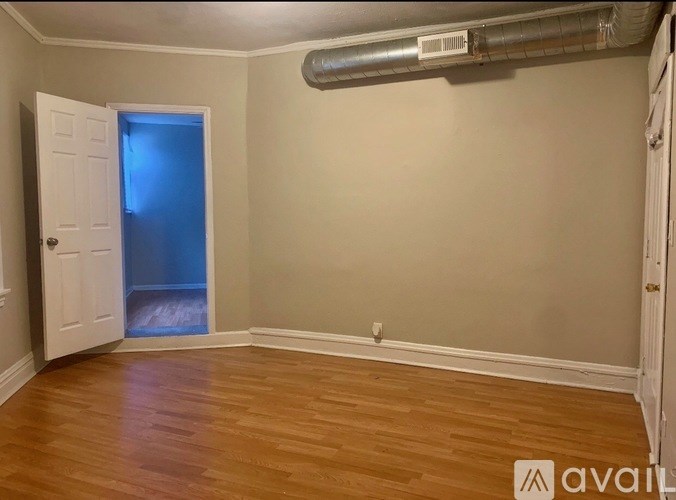 A room with wooden floors and a white door leading to another room.