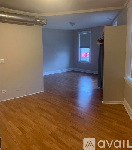 A room with wooden flooring and a window with a red sign on it.