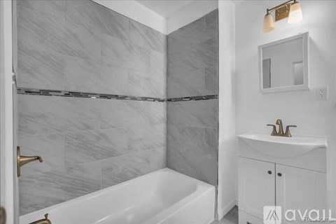 A bathroom with a white tub and a marble tile wall.