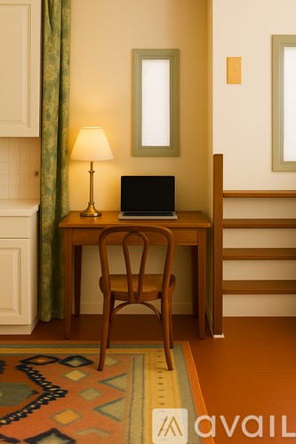 A wooden chair is in front of a desk with a laptop and a lamp.