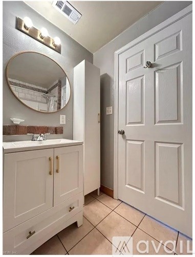 A bathroom with a white door and a round mirror above a sink.