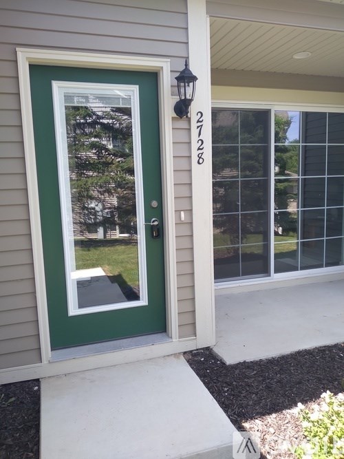 A green door with a glass window and a black lantern on the wall.