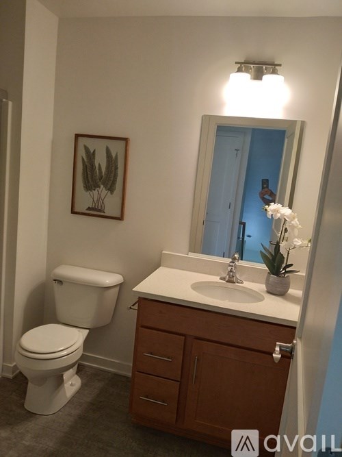 A bathroom with a toilet, sink, and a framed picture of wheat on the wall.