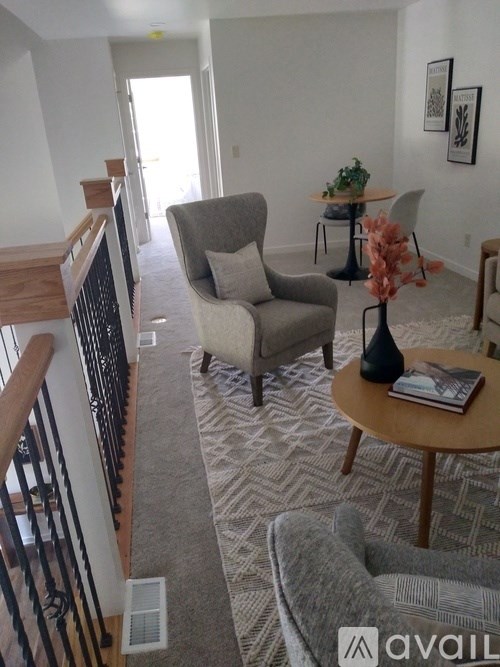 A living room with a grey couch, a grey armchair, a small table with a plant and a vase on it, and a staircase with a wooden railing.