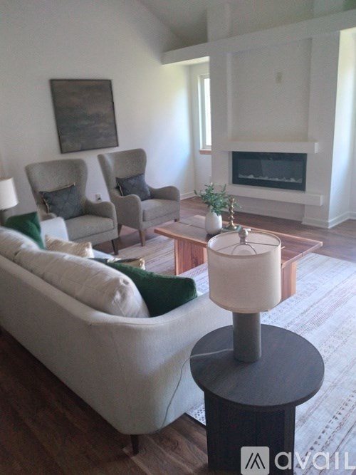 A living room with a white couch, a grey armchair, a fireplace, and a painting on the wall.