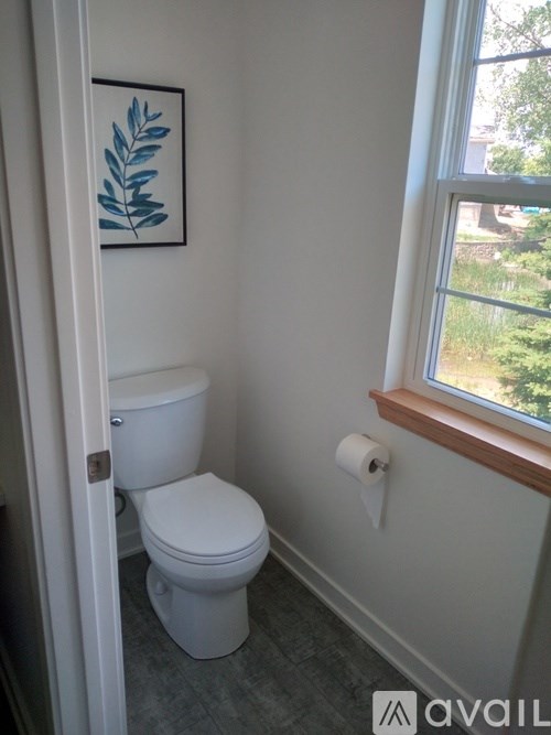 A white toilet in a bathroom with a framed picture of a leaf on the wall.