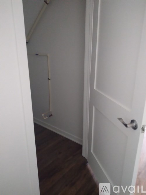 A white door with a silver handle is in a room with a white wall and a wooden floor.