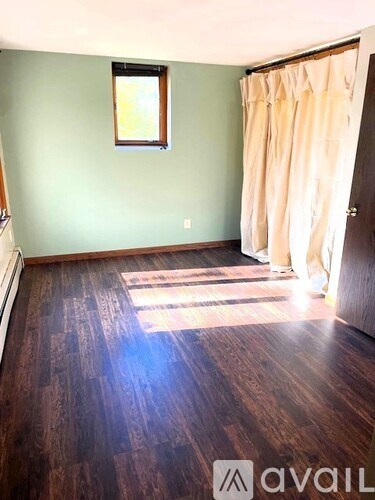 A room with wooden flooring and a window with curtains.