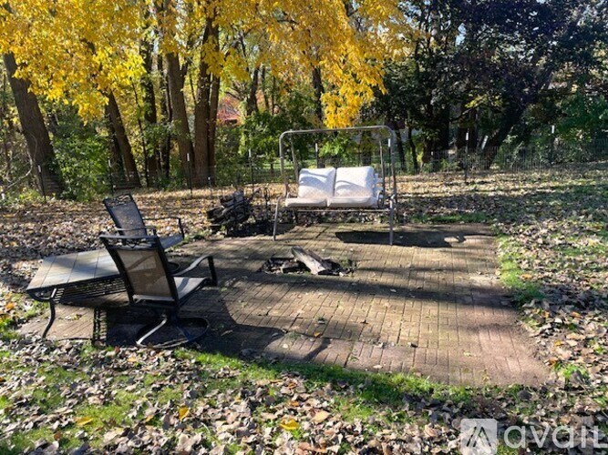 A chair and a table are on a wooden deck in a leafy area.
