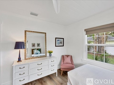 A bedroom with a pink chair and a white dresser with a mirror above it.
