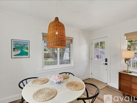 A dining room with a white table and chairs, a woven lampshade, and a framed picture on the wall.