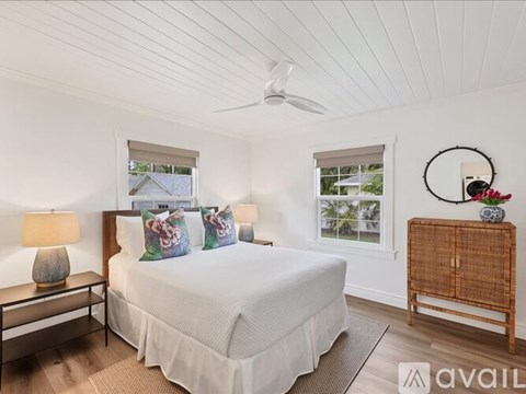 A bedroom with a large bed, a ceiling fan, and a window with a view of a house.