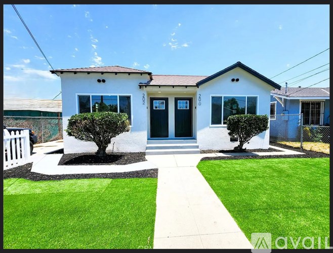 A small white house with a black door and windows is surrounded by a green lawn.