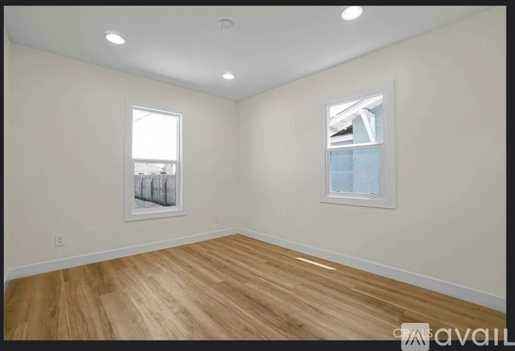 A room with wooden flooring and two windows.
