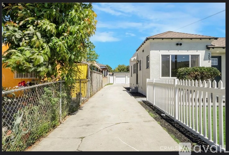 A residential street with houses on both sides and a white picket fence on the right.