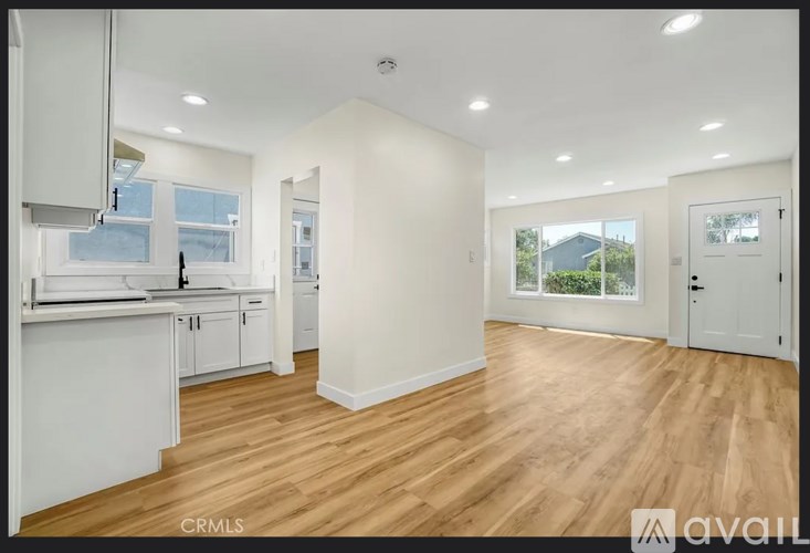 A well-lit, spacious kitchen and living room with wooden flooring and white cabinetry.
