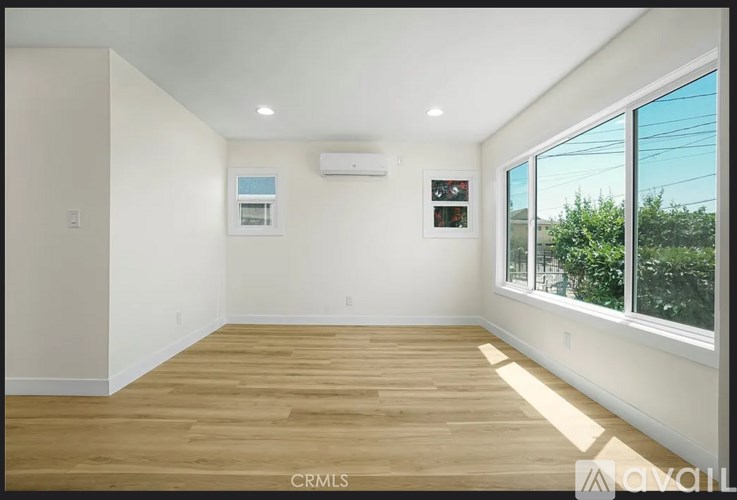 A room with wooden flooring and a window overlooking a green area.