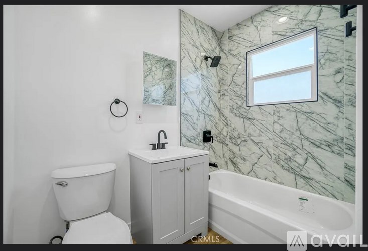 A white toilet sits next to a white bathtub in a bathroom with marble walls.