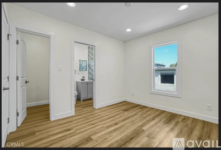 A room with wooden floors and white walls, with a window showing a building outside.