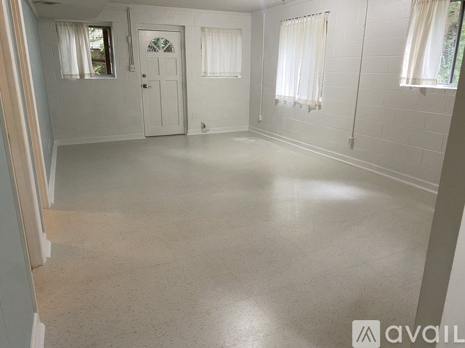 A spacious room with a door, two windows with curtains, and a wall with a window.