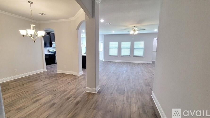 A spacious room with wooden flooring and a chandelier hanging from the ceiling.