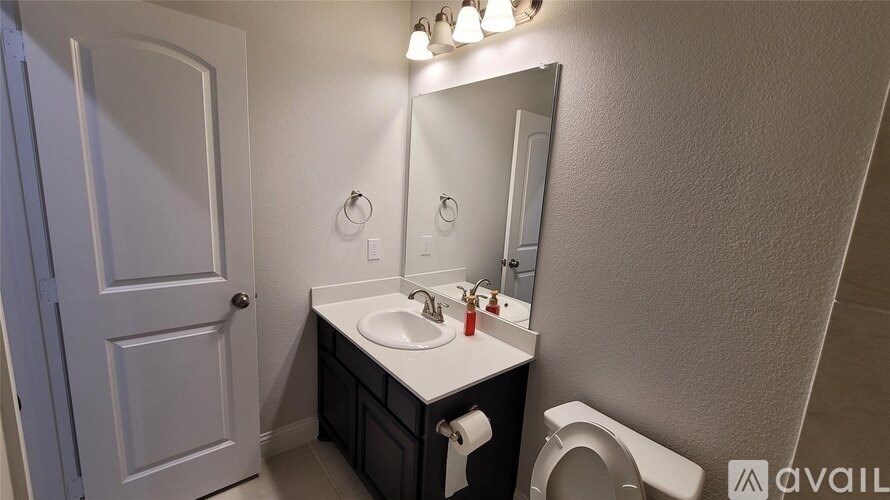 A bathroom with a sink, mirror, toilet and a door.