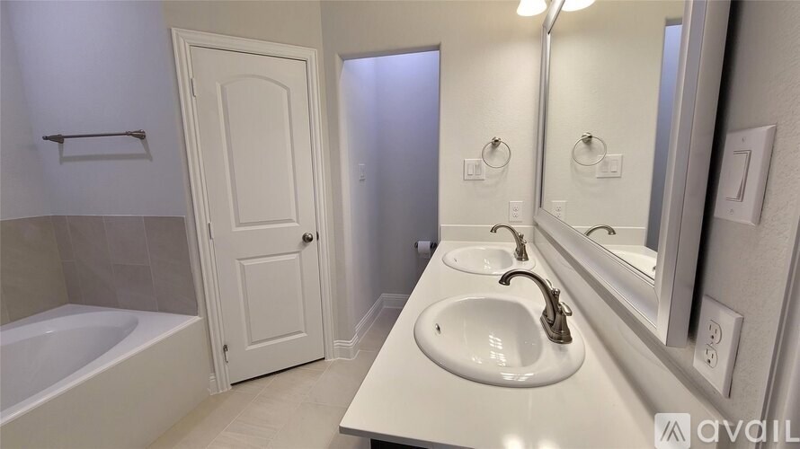 A white bathroom with a tub, sink, mirror and towel rack.