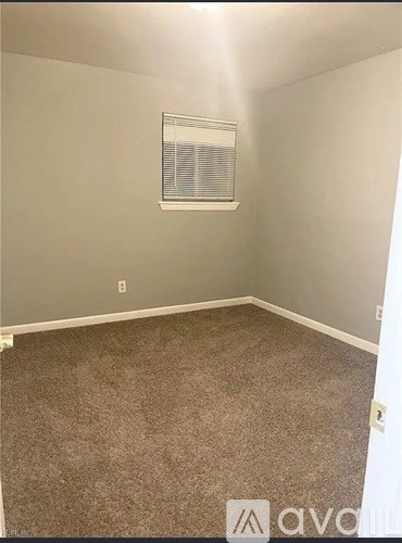 A room with a carpeted floor and a window with blinds.