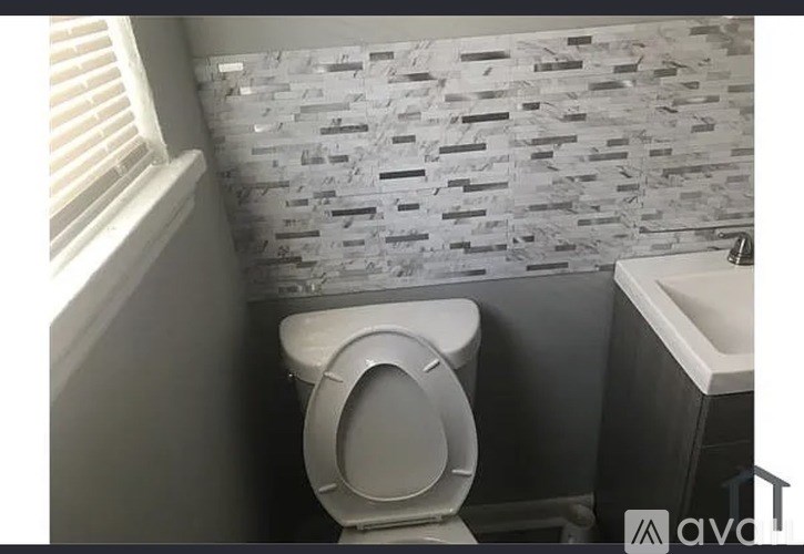 A white toilet in a bathroom with a grey tiled wall.