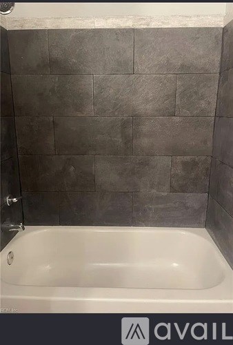A bathroom with a white tub and grey tiled walls.