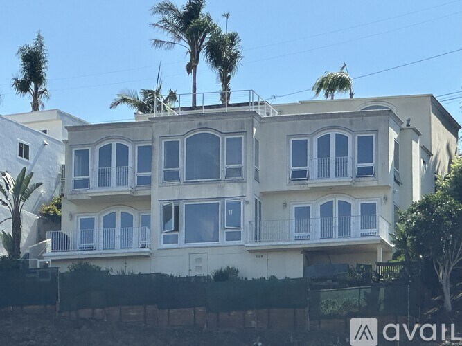 A white two-story building with balconies and palm trees in front.